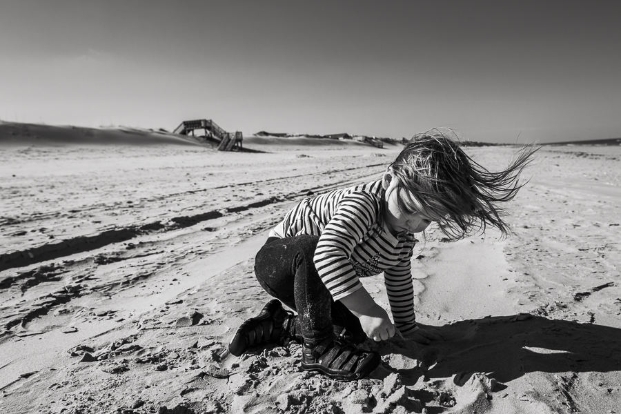 little girl playing on the beach alone in the wind