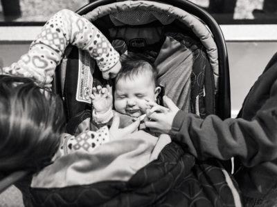 Big brother and big sister touching sleeping baby in car seat