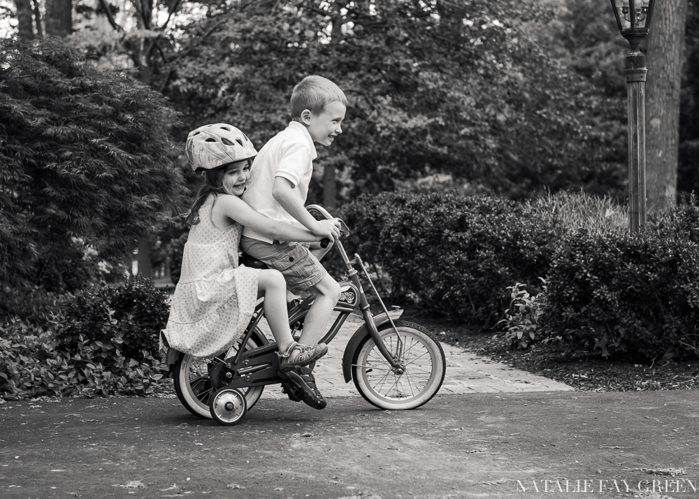 Little sister riding on the back of big brother's bicycle